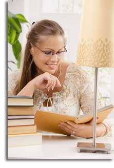 Woman wearing glasses and a white blouse reading and smiling next to a lamp