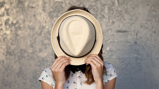 young woman hiding face behind straw hat